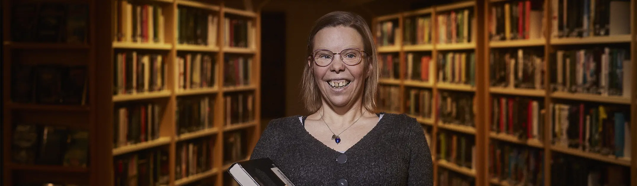 En kvinna med funktionsnedsättning står i ett bibliotek.